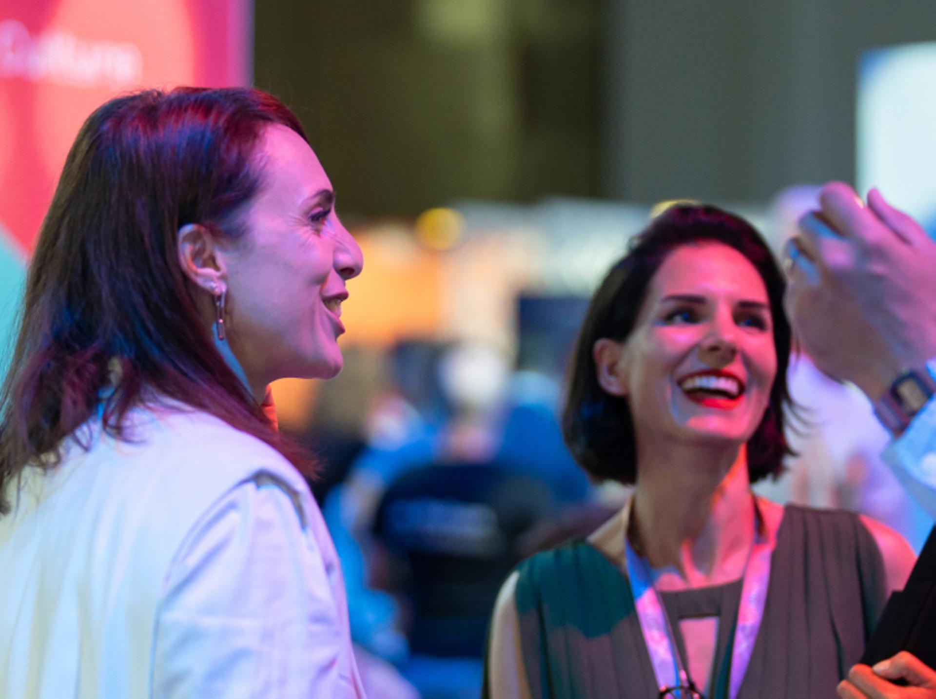 A photograph of two women engaged in conversation, laughing. 