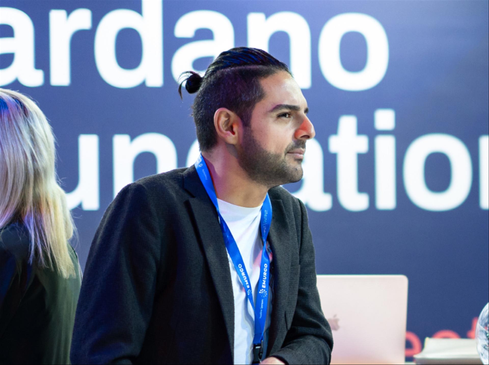 A photograph of an individual engaged in a discussion at the Cardano Foundation booth. 